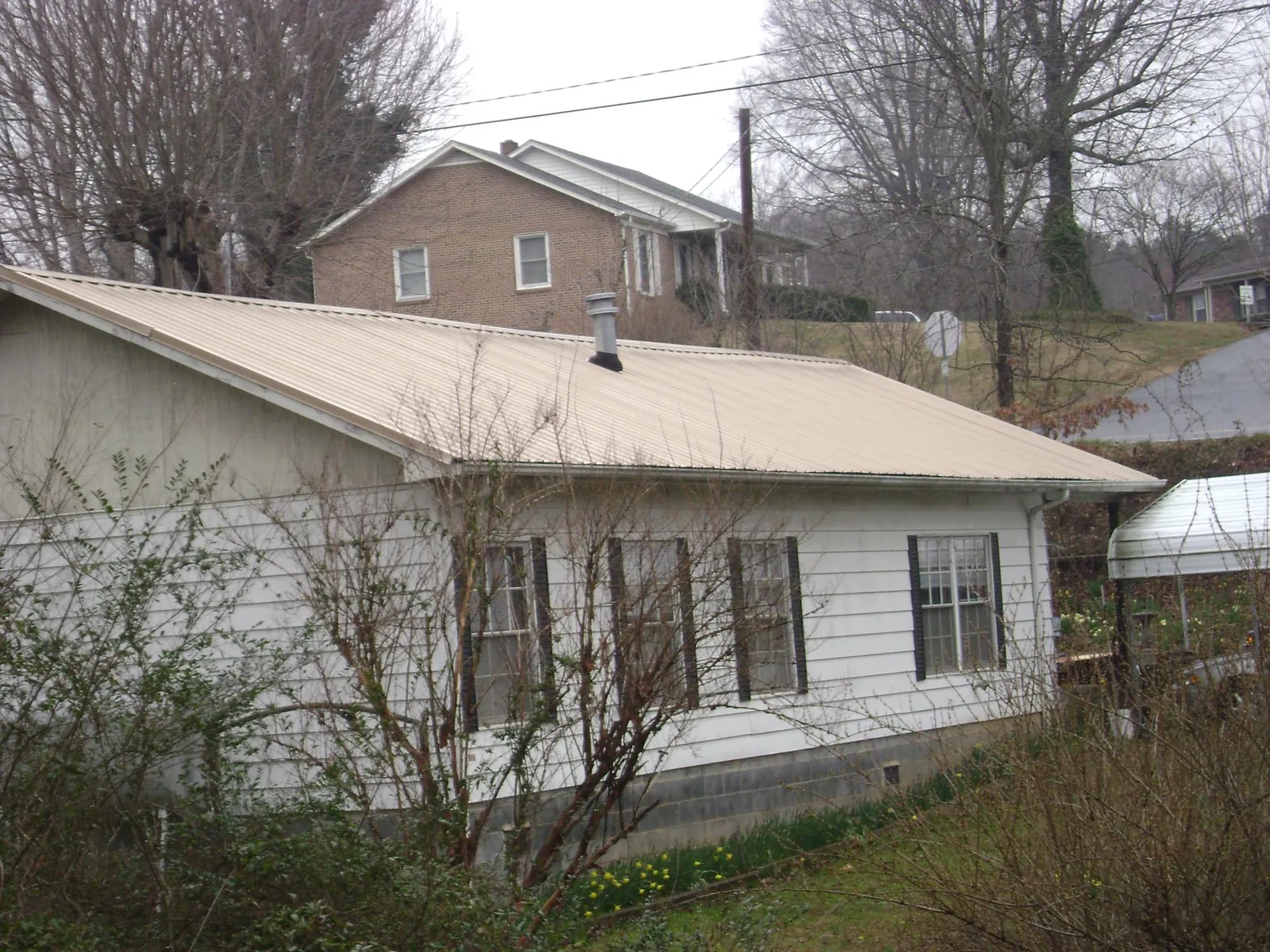 Tan metal roof on a white sided house set into a hillside — Commercial Roofing by Roofing Brothers in Port Republic